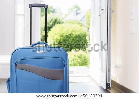 Blue vacation suitcase by opened front door.