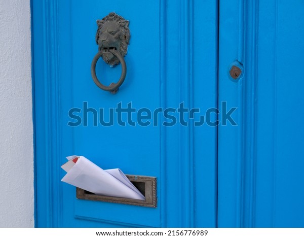 Blue vintage door\
with a knocker in the shape of a lion, mailbox slot in the door\
with advertising\
newspapers.