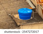 Blue water tank installed on top of a building or residence, in a concrete structure. Reservoir used for storing water.