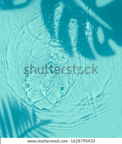 Blue water texture background on the noon sunlight with tropical leaves shadow. 
