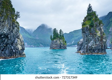 Blue waters and tree covered rocks jutting out of water on a cloudy morning at Porcupine bay at Kenai Fjords National Park, Alaska