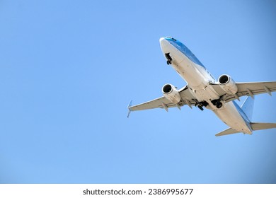 blue and white aircraft photographed from below shortly after takeoff, copyspace on the left side of the image, the landing gear is in the process of folding in - Powered by Shutterstock