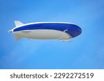 A blue and white airship with passengers on board flies against the blue sky. 