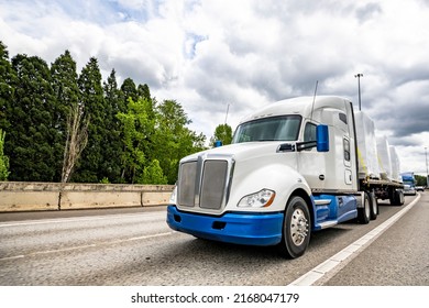 Blue and white big rig bonnet industrial semi truck tractor transporting covered fastened commercial cargo on flat bed semi trailer driving for delivery on the wide multiline turning highway road - Shutterstock ID 2168047179