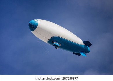 Blue And White Blimp On A Sunny Day Floating With A Blue Sky Background.