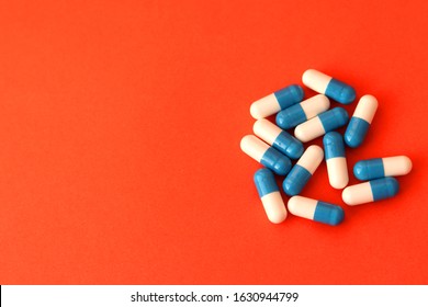 Blue And White Capsules With Antiviral Medication On A Red Background. Selective Focus. Course Of Treatment.