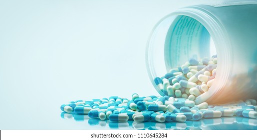 Blue and white capsules pill spilled out from white plastic bottle container. Global healthcare concept. Antibiotics drug resistance. Antimicrobial capsule pills. Pharmaceutical industry. Pharmacy.