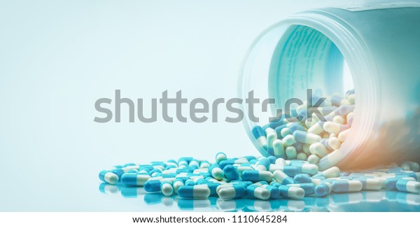 Blue and white capsules pill spilled out from\
white plastic bottle container. Global healthcare concept.\
Antibiotics drug resistance. Antimicrobial capsule pills.\
Pharmaceutical industry.\
Pharmacy.