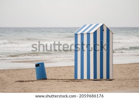 Blue and white changing cabin in the middle of an empty beach on a cloudy day