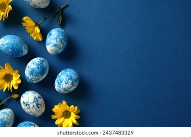 Blue and white Easter eggs with yellow flowers on dark blue background. Happy Easter concept