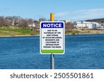 A blue and white metal sign with a notice: Due to an outbreak of the H5N1 strain of avian influenza, residents are cautioned to refrain from feeding the birds. The background is blue water and trees.