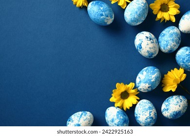Blue and white painted Easter eggs on dark blue background with yellow flowers. Flat lay, top view, copy space