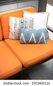 Blue And White Pattern Throw Pillows On An Outdoor Patio Chair, With An Orange Couch Cushion Bench, On A Backyard Deck