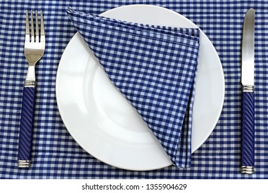 Blue And White Table Or Picnic Place Setting. Plate, Knife And Fork And Napkin On A Blue Gingham Table Cloth.