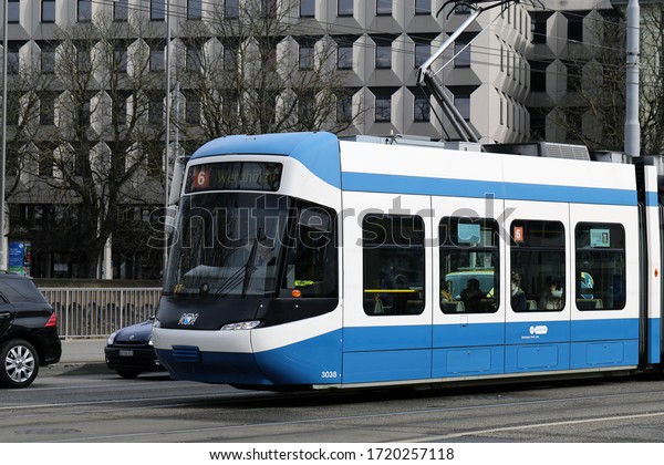 Blue and white tram moving in downtown Zürich,\
Switzerland, March 2020. Trams are a form public transportation in\
many big cities in Switzerland. Color image with some street, cars\
& buildings in it.