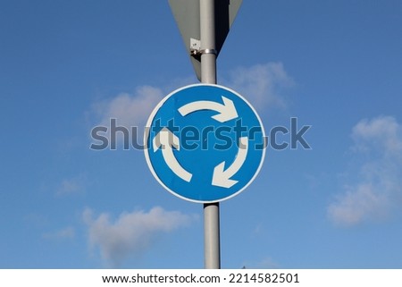 Blue and White U.K. Clockwise Roundabout Road Sign on Blue Sky Background