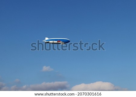 A blue and white zeppelin flies in the sky