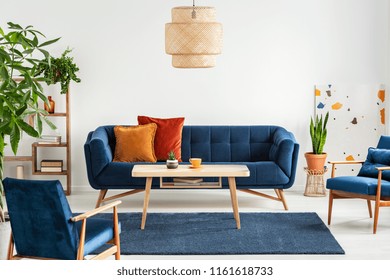 Blue Wooden Armchairs And Couch In Living Room Interior With Plants And Lamp Above Table. Real Photo