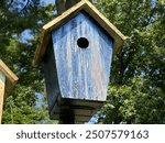 Blue wooden birdhouse on a post with trees full of leaves