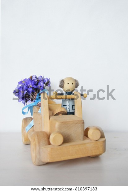 A blue wooden car with\
wooden toy man inside and blue flowers. White background. Place for\
your text.
