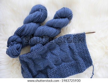 Blue wool knitting blanket in progress with yarn hank and needles