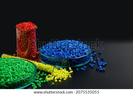Blue, yellow, red granules of polypropylene, polyamide in a test tube and a petri dish. Black background. Plastic and polymer industry, industry. Microplastic products.