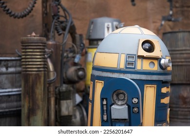 Blue and yellow robot droid with robots and a wall behind it