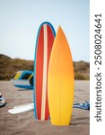 Blue and yellow surfboards standing upright on the beach with white fins, summer seaside scene