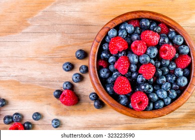 Blueberries And Raspberries In A Wooden Bowl On Old Wood Background