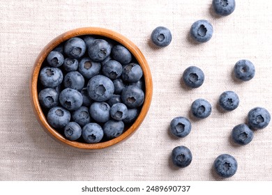 Blueberries in a wooden bowl on linen fabric. Dark blue colored, ripe, raw berries, fruits of Vaccinium corymbosum, cultivated blueberries of the northern highbush blueberry. From above, food photo. - Powered by Shutterstock