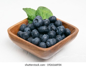 Blueberry berries with mint leaves are in a wooden plate. White textured background