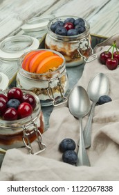 Blueberry, Cherry And Apricot Parfaits In Mason Jars, On A Rustic Wood Background. Healthy Still Life Concept Food. Yogurt And Fresh Summer Fruits Parfait 