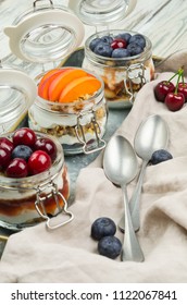 Blueberry, Cherry And Apricot Parfaits In Mason Jars, On A Rustic Wood Background. Healthy Still Life Concept Food. Yogurt And Fresh Summer Fruits Parfait 