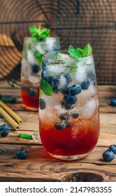 Blueberry ice mojito with mint in tall glasses on rustic wooden background. Selective focus