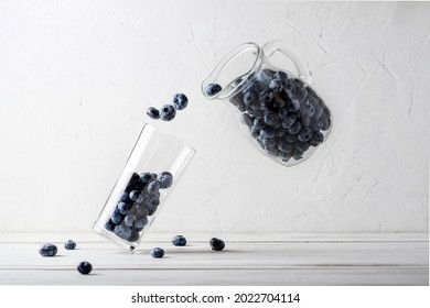 Blueberry Levitation. Blueberries From A Jug Are Poured Into A Glass Beaker On A White Background. Making A Berry Smoothie. Abstract Creative Concept.