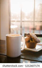 A Blueberry Muffin And A Cup Of Coffee Latte On A Wood Table With Rays Sunlight.