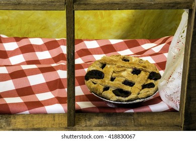 Blueberry Pie On Checked Table Cloth Cooling On Wood Framed Window Sill With Yellow Background