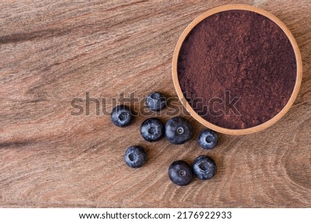 Blueberry powder in wooden bowl and fresh blueberries fruit isolated on wooden table background, top view, flat lay.