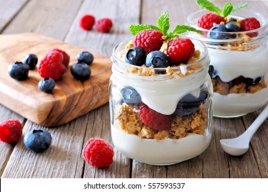 Blueberry and raspberry parfaits in mason jars, scene on a rustic wood background