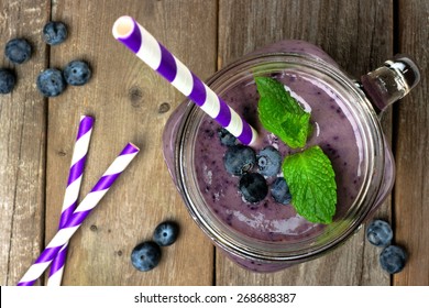 Blueberry smoothie with mint in mason jar mug with straw. Overhead view on wood.