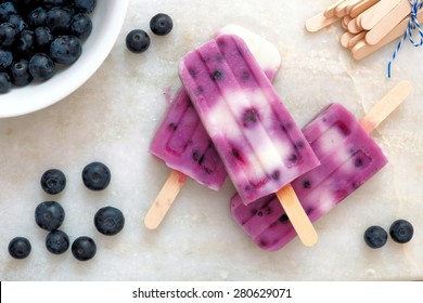 Blueberry vanilla popsicles in a cluster with fresh berries on a white marble background