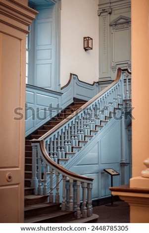 A blue-colored ornate and antique staircase leads to a second floor in an old historic building.