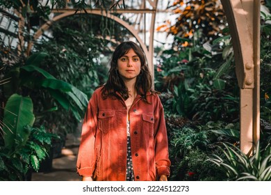 blue-eyed brunette caucasian girl in red jacket standing with arms outstretched calm and relaxed among the pretty houseplants in the botanic garden, botanic garden christchurch, new zealand - Shutterstock ID 2224512273