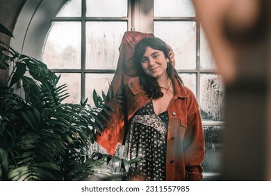 blue-eyed caucasian young woman in a pretty red jacket with earrings in her ears looking at the camera happy content calm and relaxed next to the plants of the botanic garden, botanic garden - Shutterstock ID 2311557985