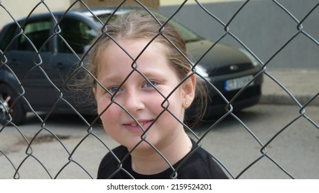 a blue-eyed european girl smiling from behind a wire mesh