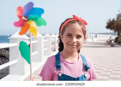 Blue-eyed girl holding a moving colored windmill. Concept: lifestyle, beach day, walk by the sea