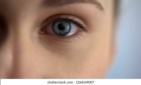 Blue-eyed woman checking eyesight at ophthalmologist in clinic, looks at camera