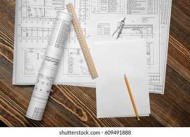 Blueprints on wooden table background with a pencil, a ruler and compasses lying beside. Engineering and design. Construction projects. Planning.