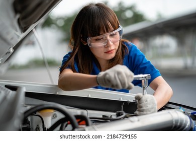 A Blue-shirted Asian Female Handyman Is Doing A Car Repair Service In The Center. Auto Repair Concept. Car Repair Service Center Happy Female Mechanic In Auto Repair Garage