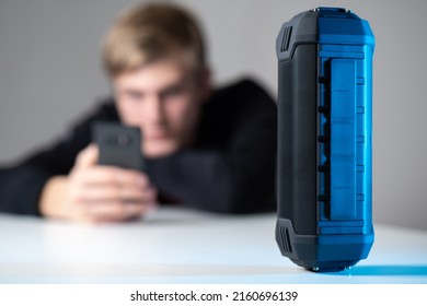 Bluetooth speaker close-up. Wireless speaker on the background of a blurry image of a man with a smartphone. The young man controls the Bluetooth speaker from the phone. Audio playback.